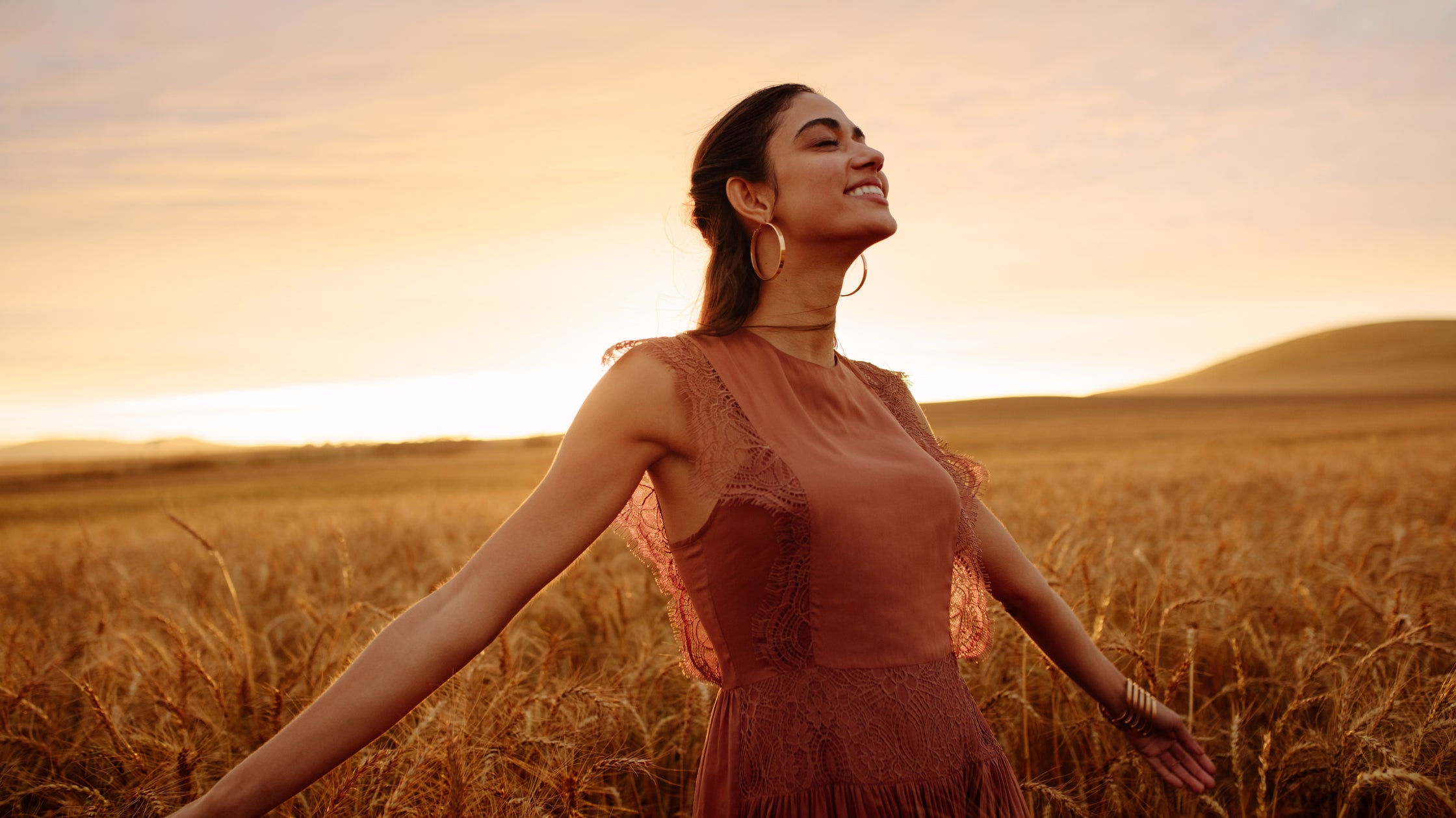 A happy model walking through a wheat field at sunset, symbolizing the joy of using Baily Cosmetics' Leaping Bunny certified, cruelty-free products.